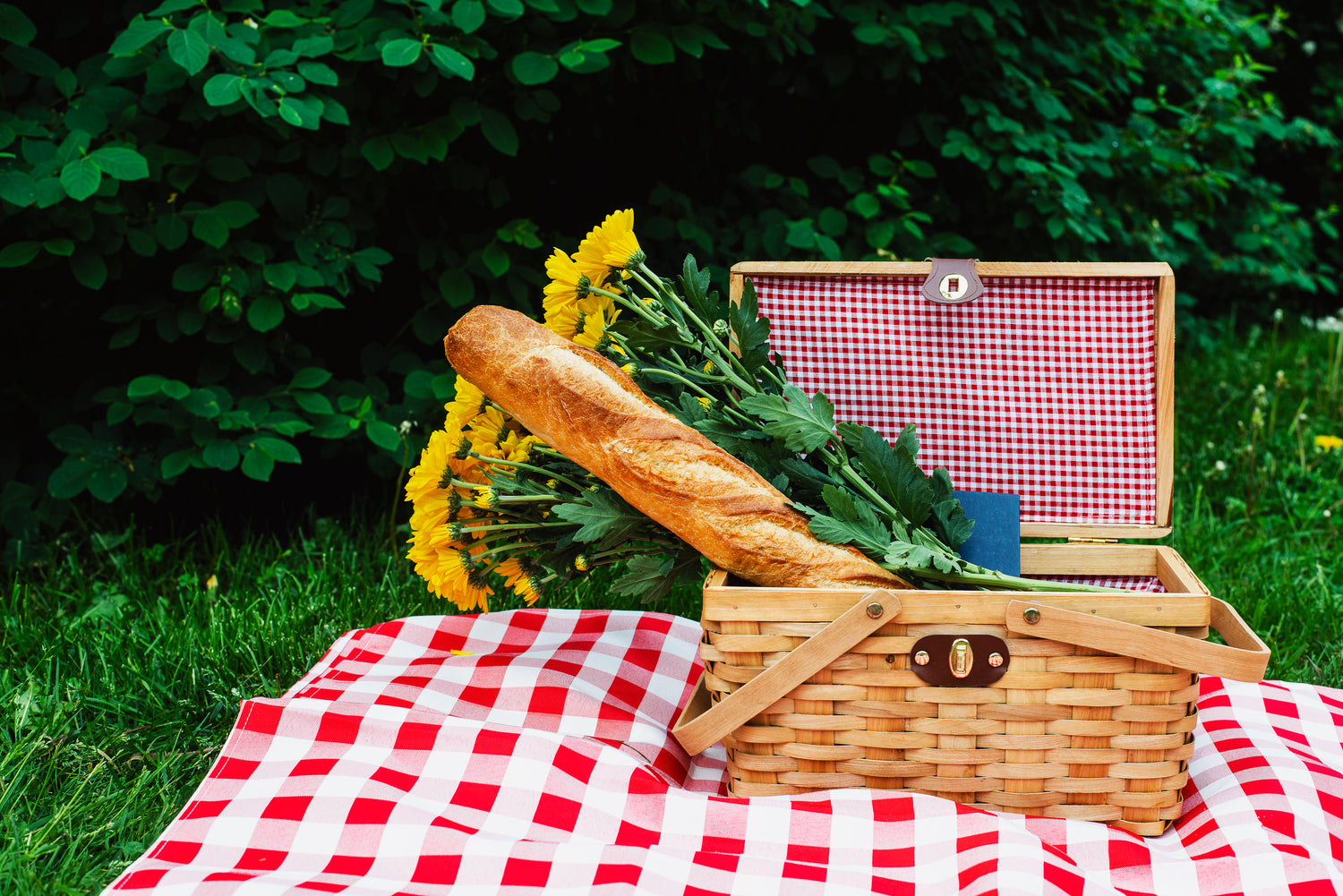 baguette and flowers in basket on picnic blanket
